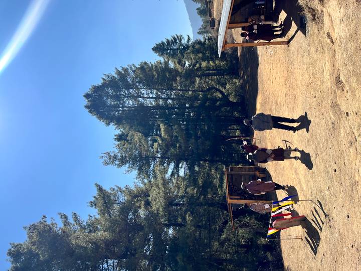 Bhutanese archers in traditional dress take aim on a sunny forest clearing.