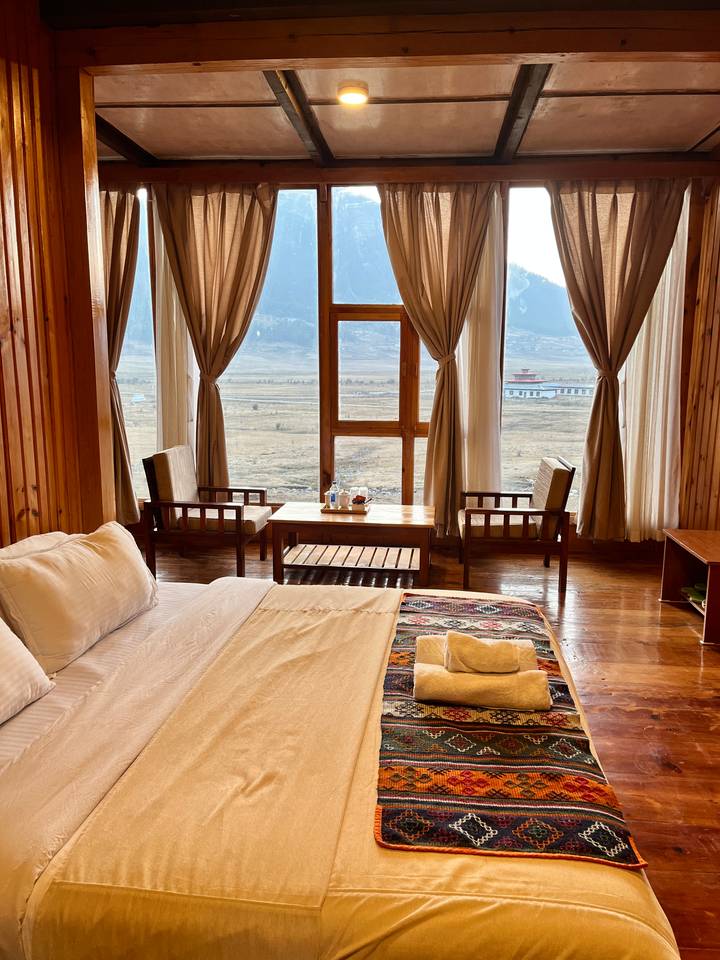 Warm wooden hotel room with large windows framing a tranquil river valley landscape.