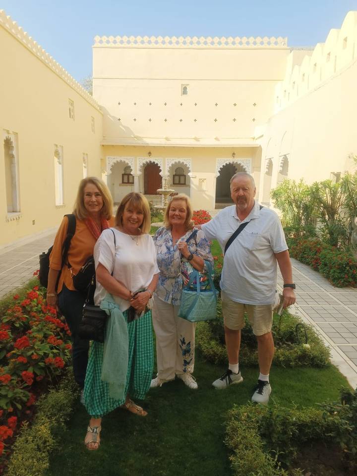 Small group of travellers posing in a sunny courtyard filled with red flowers.