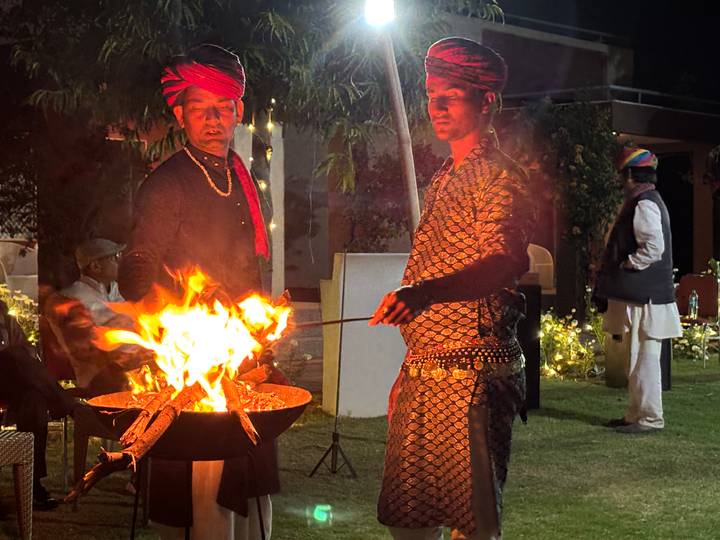 Rajasthani performers in traditional turbans tending a bonfire during an outdoor evening event.