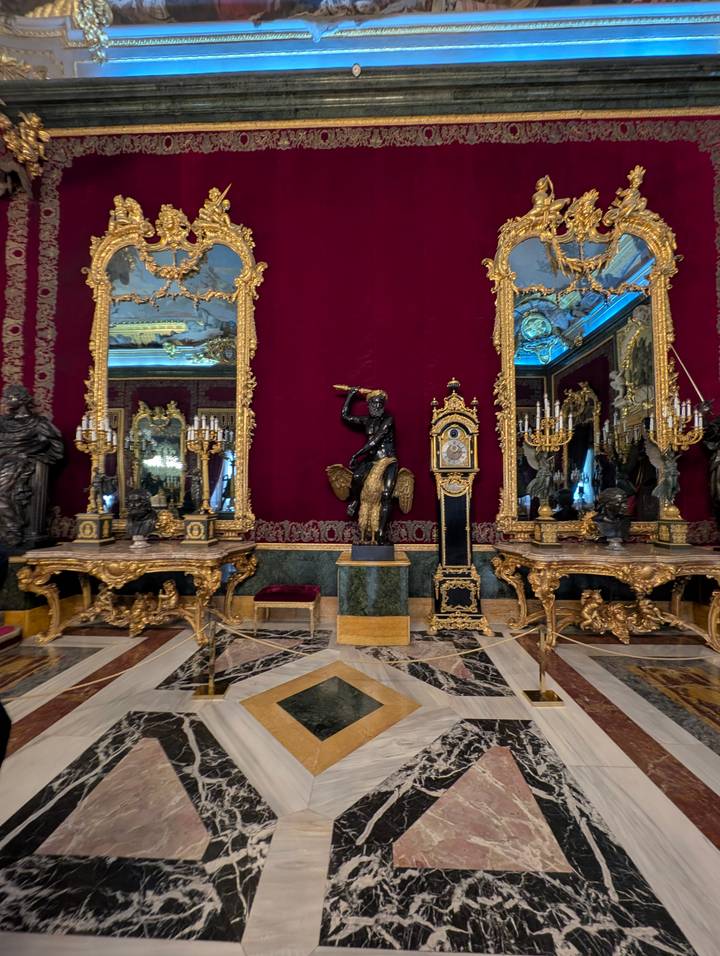 Lavish red-and-gold palace room filled with ornate clocks, mirrors and candelabra.