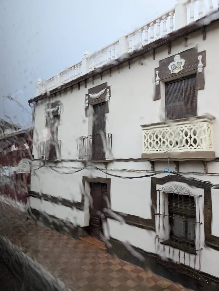 Street view distorted by raindrops on a vehicle window, blurring the scene.