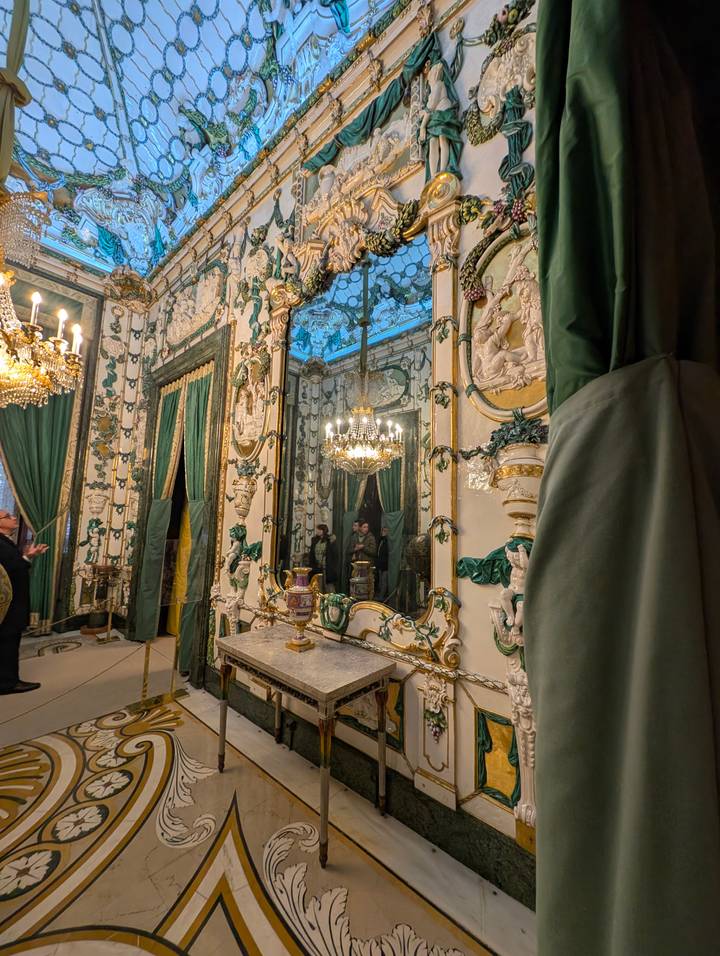 Opulent mirror-lined salon with chandeliers, marble floors and ornate green drapery.