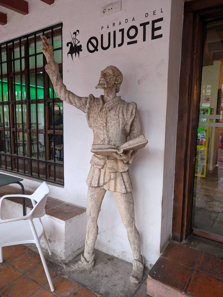Stone statue of a medieval figure holding a book outside a small café.