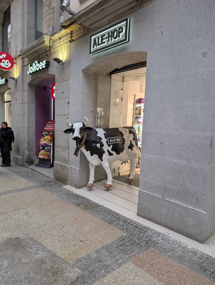 Life-size spotted cow statue outside a shop entrance on a pedestrian street.