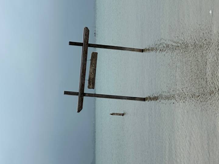 Lonely wooden swing frame standing in calm, misty coastal waters on an overcast day.