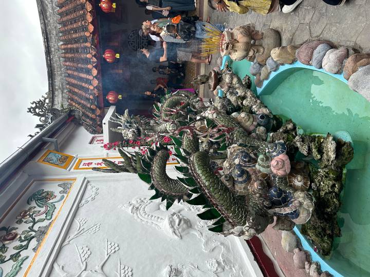 Ornate metal dragon fountain surrounded by incense smoke in a temple courtyard while visitors observe.