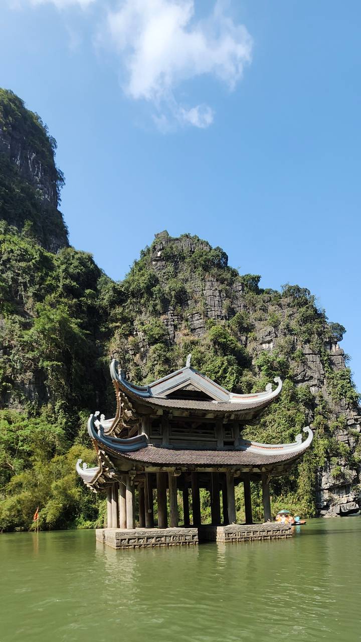 Traditional Vietnamese temple roof set against towering limestone karst cliffs covered in lush greenery.