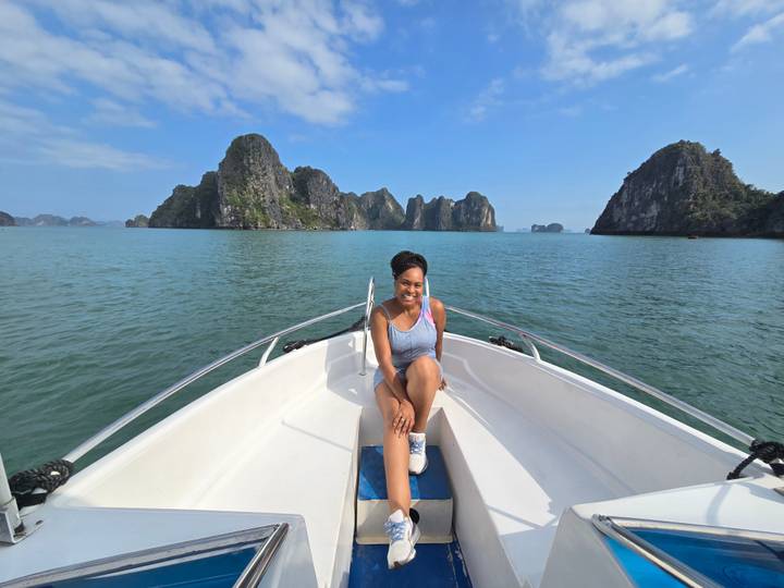 A smiling traveler sits at the bow of a boat surrounded by Halong Bay’s towering limestone islands.