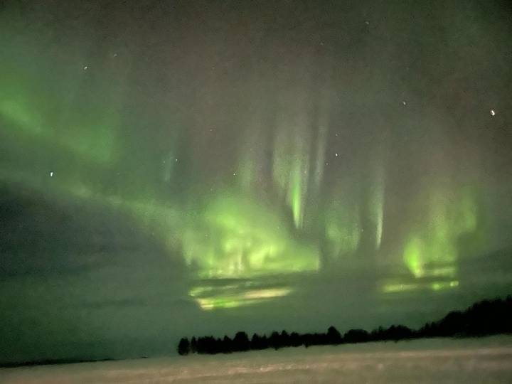 Green aurora borealis curtains ripple across a dark arctic sky dotted with stars.