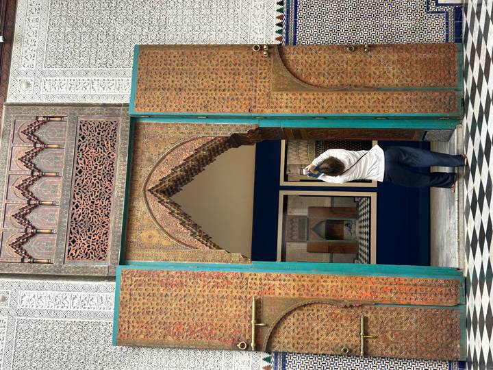 Visitor photographs ornate Moroccan doorway framed by coloured tile panels and checkerboard floor