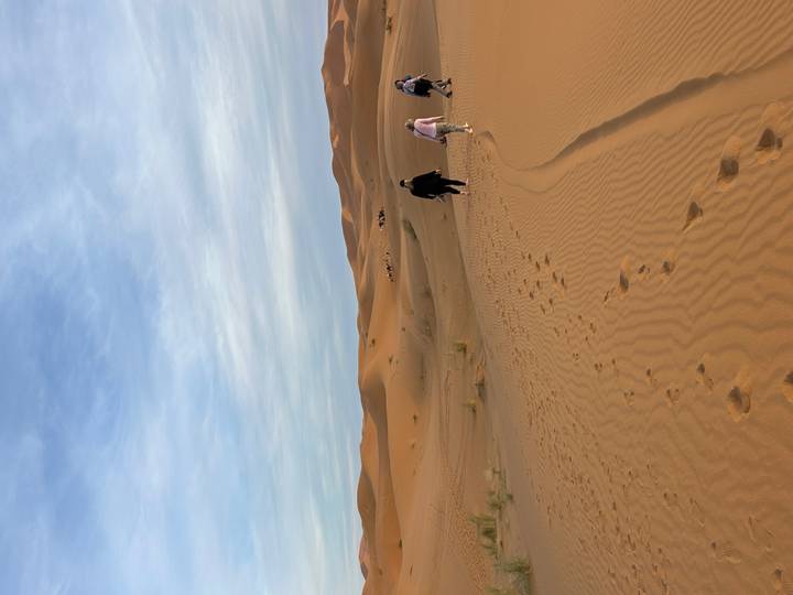 Hikers crossing vast sandy dunes beneath a pale morning sky in the Sahara