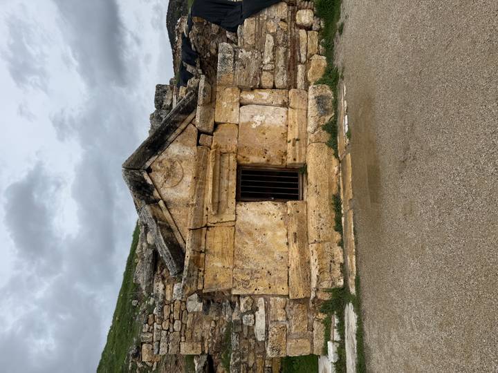 Small stone tomb with barred window set into an ancient wall under cloudy skies.