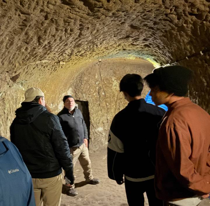 Tour guide speaks to visitors inside a dimly lit underground cave passage.