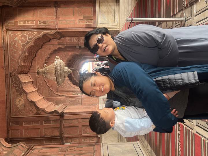 Three-generation family poses inside a richly carved mosque corridor under a sparkling chandelier.