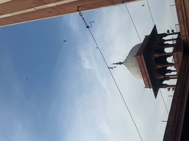 Silhouette of a Mughal dome against blue sky with birds and overhead wires.