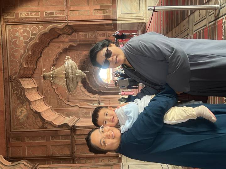 Mother and grandmother holding a smiling toddler inside an ornate mosque hallway.