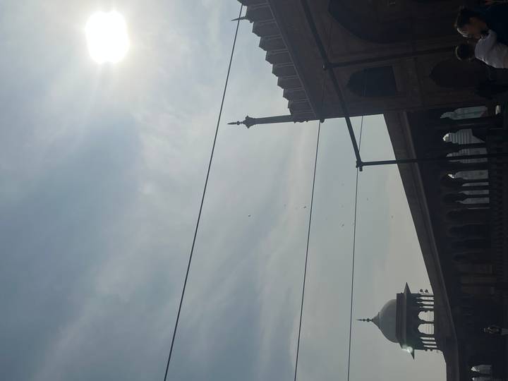 Back-lit view of a mosque courtyard, silhouetted minaret and tangled power lines under hazy sun.