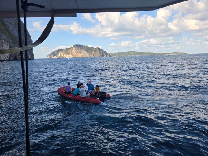 Inflatable red dinghy carrying tourists across deep blue waters with limestone islands of Phi Phi in the distance.