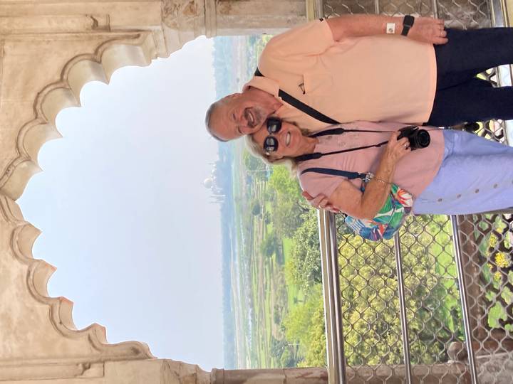 Couple embracing inside a fort balcony with distant view of the Taj Mahal across green plains