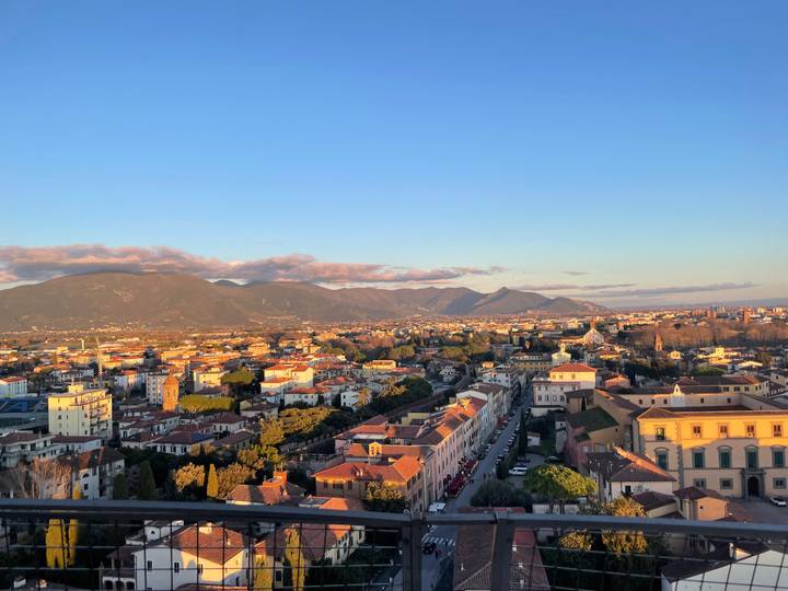 Wide cityscape of Pisa with distant mountains under warm late-day light