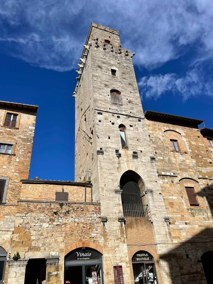 Tall medieval stone tower and adjacent buildings against vivid blue Tuscan sky