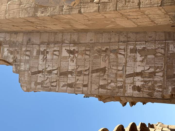 Tall sandstone temple wall richly carved with vertical rows of ancient Egyptian reliefs against a clear blue sky.