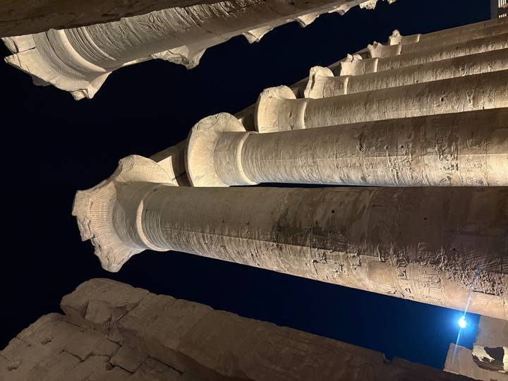 Row of towering illuminated columns of an ancient Egyptian temple dramatically lit against the night sky.