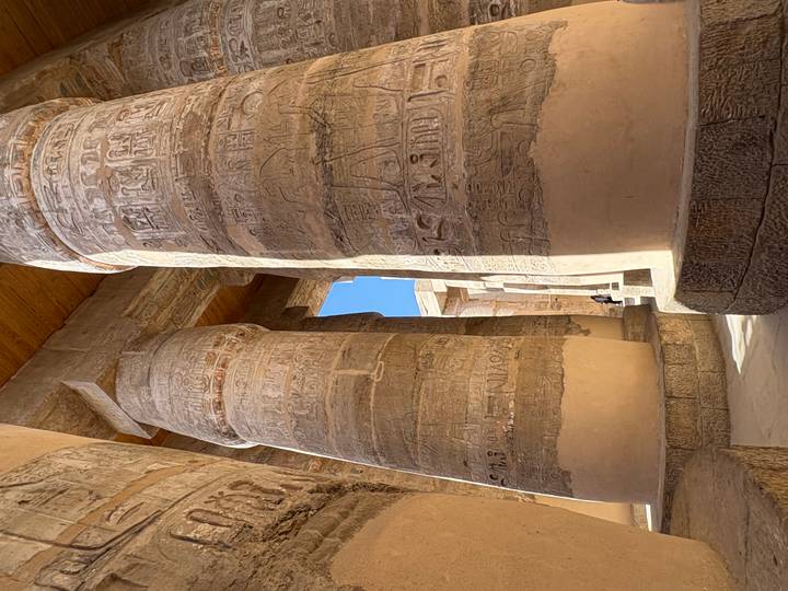 Monumental stone columns covered in hieroglyphs towering inside an ancient hypostyle hall.
