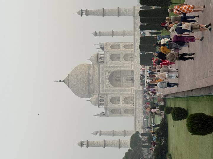 Front view of the Taj Mahal with crowds on the garden pathway under hazy skies.