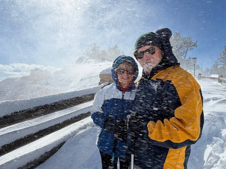 Couple braving blowing snow with goggles and winter jackets at a canyon viewpoint.