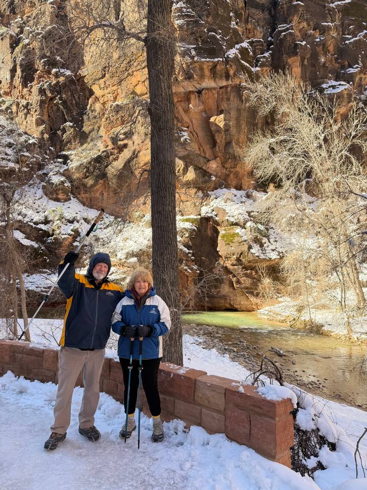 Couple smiles beside a snowy canyon stream with sunlit cliffs in the background.