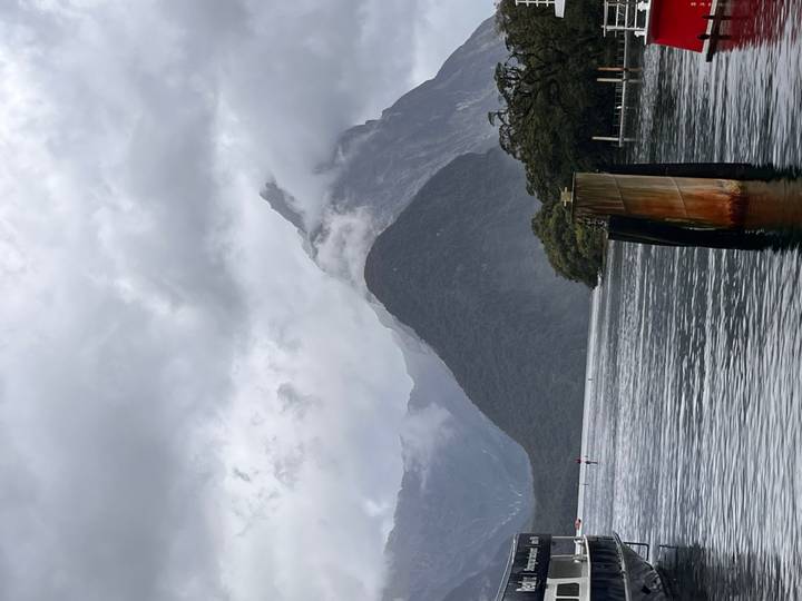 Dramatic view of Mitre Peak emerging through low clouds above the calm fjord waters of Milford Sound.