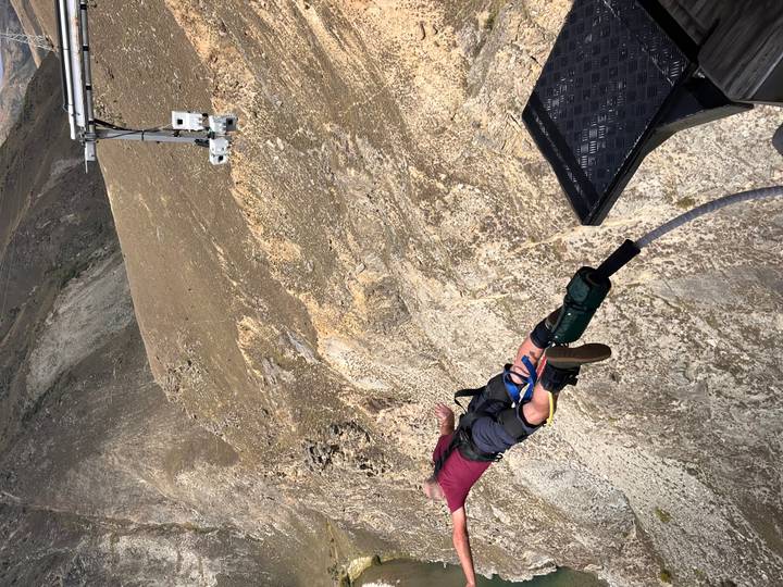 Person diving head-first from a platform on a bungee cord above a rocky canyon.