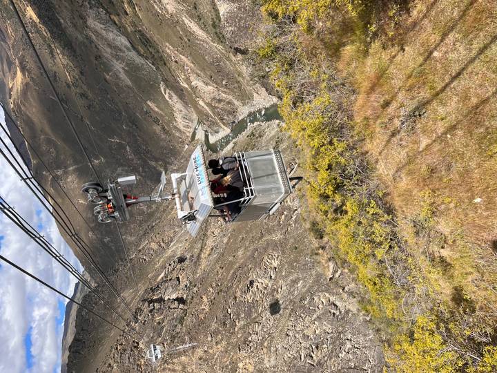 Open cable car suspended over a deep river canyon carrying thrill-seekers.