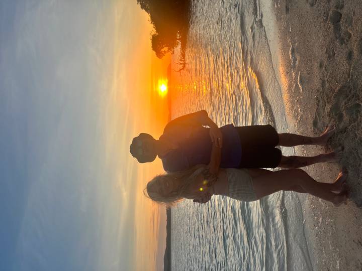 Couple embracing on the shoreline with a vivid orange sun setting over calm sea
