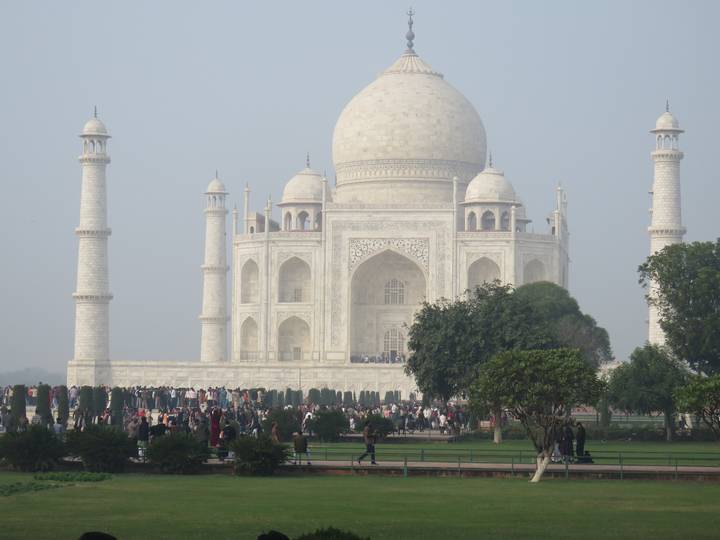 Iconic white marble Taj Mahal framed by minarets with crowds gathered on the forecourt.