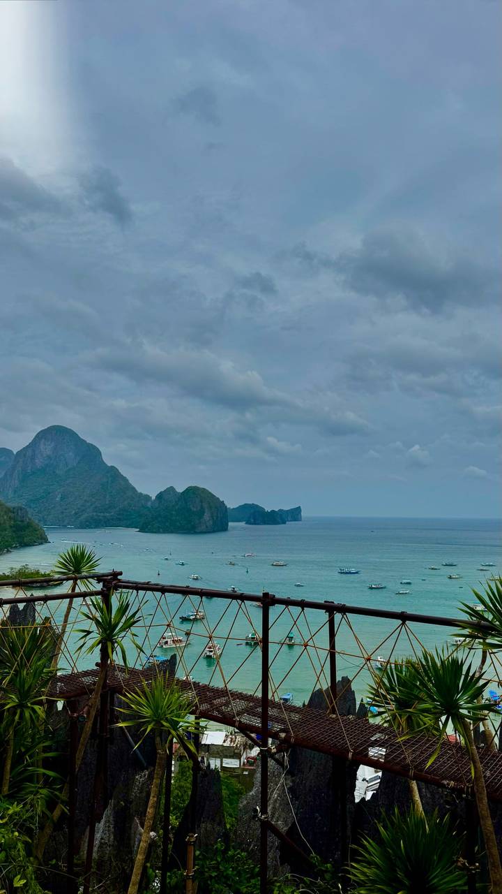 Cloudy seascape of dramatic limestone islands and turquoise bay waters dotted with boats.