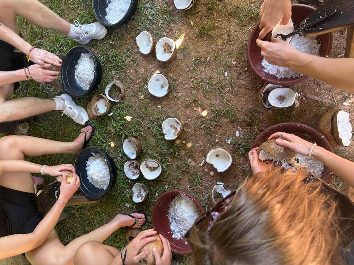Travelers grate fresh coconut into bowls during an outdoor cooking demonstration.
