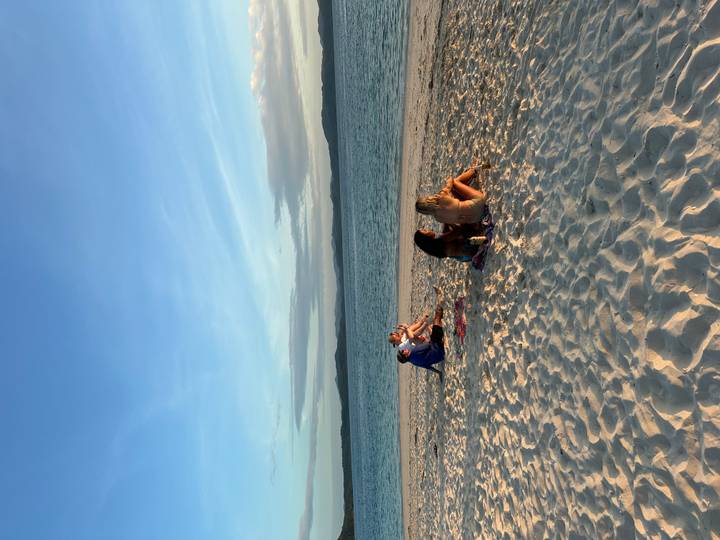 Small group relaxes on white-sand beach as the sun lowers over a calm sea.
