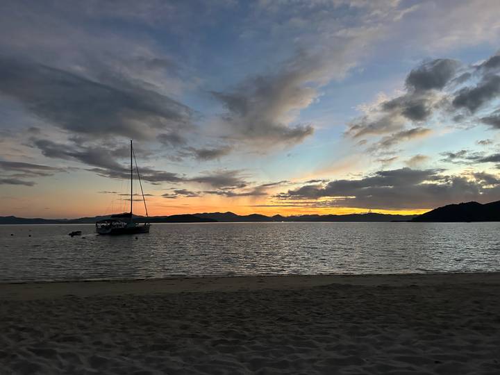 Sailboat anchored off a quiet beach under colourful post-sunset clouds.