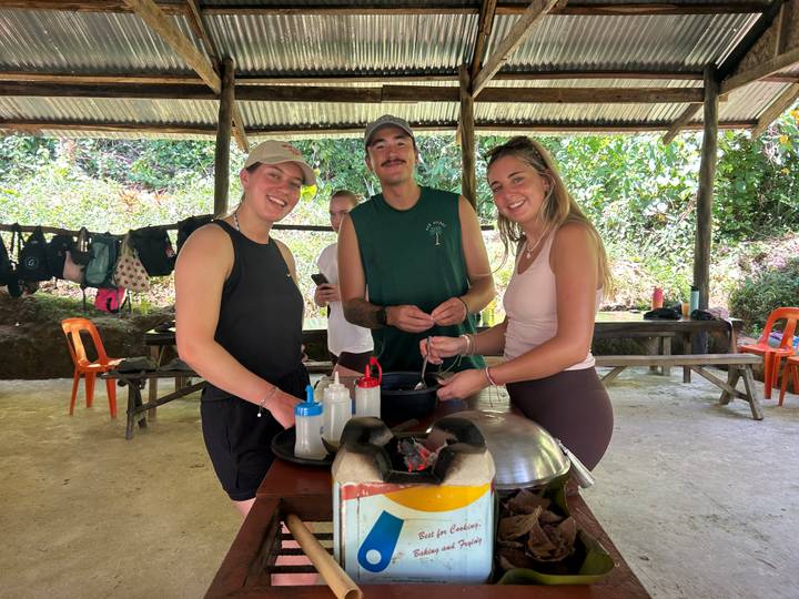 Travelers smiling while preparing food together at an open-air cooking station in a jungle setting