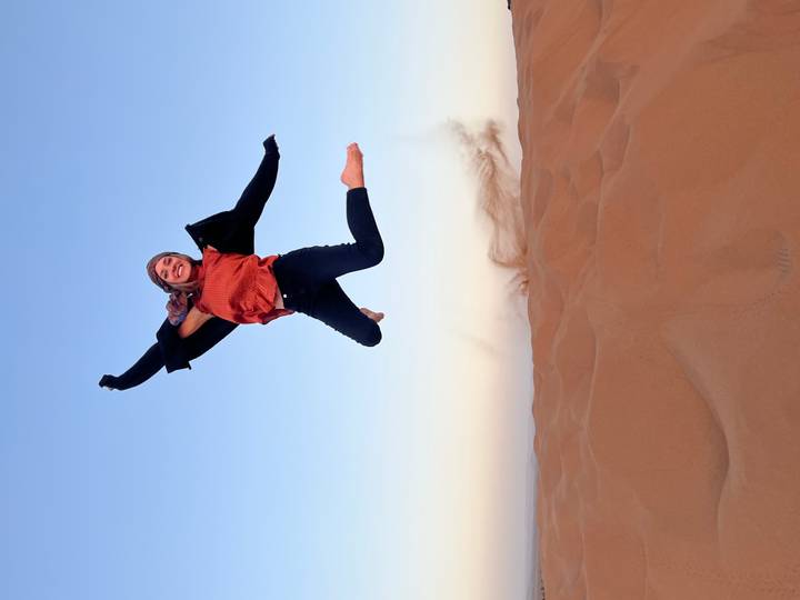 Young traveller caught mid-air jumping over golden Sahara dunes at sunrise.