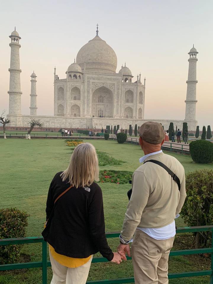 Two travellers admire the Taj Mahal from the lush morning gardens with soft sunrise light.