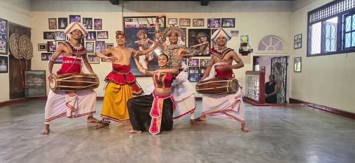 Traditional Sri Lankan dancers in colorful costume performing indoors.