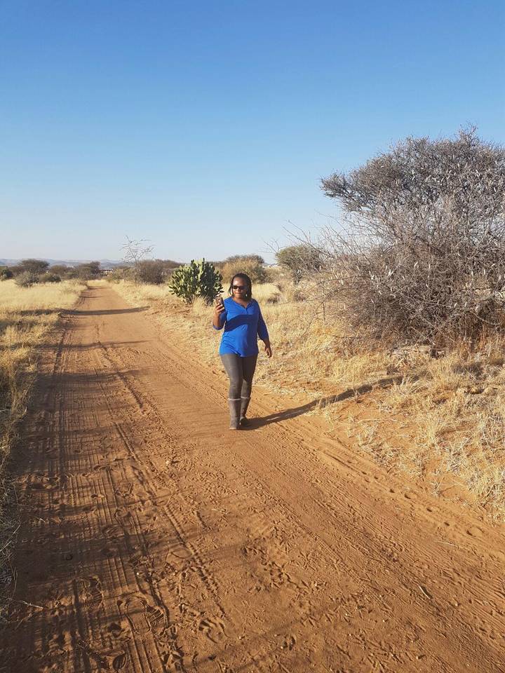 Woman walking along a dusty track through dry Namibian savannah.