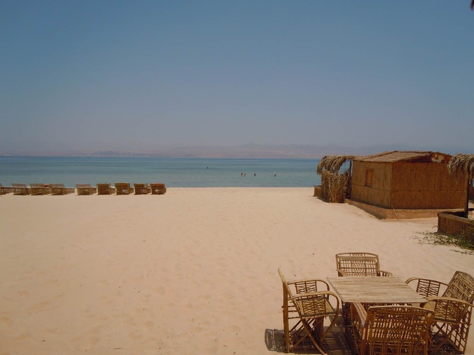 Une plage de sable avec des abris de paille et des chaises longues.