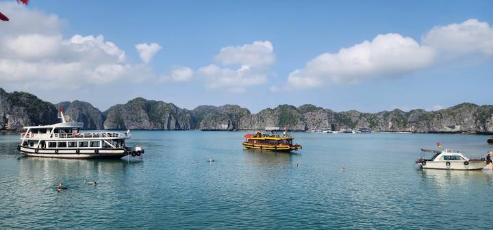 Calm turquoise waters with small boats and dramatic karst backdrop in Ha Long Bay.