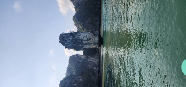 Tall limestone karst pillar rising from emerald waters in Ha Long Bay.