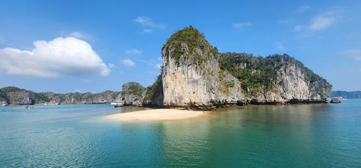 A small white-sand beach and limestone island surrounded by clear blue water in Ha Long Bay.